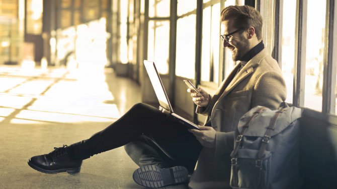 Working man sitting on the floor with a laptop and a smartphone as a symbol for optimal audience reach Working man sitting on the floor with a laptop and a smartphone as a symbol for optimal audience reach